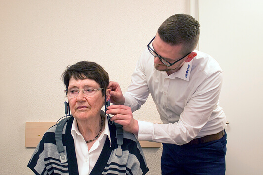 Ein Hörakustiker passt einer Seniorin ein Hörgerät zur Hörverbesserung an.