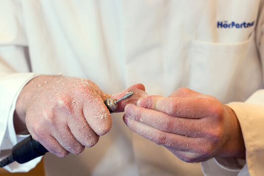 Ein Hörakustiker passt ein Hörgerät mit einem Schleifwerkzeug individuell an.